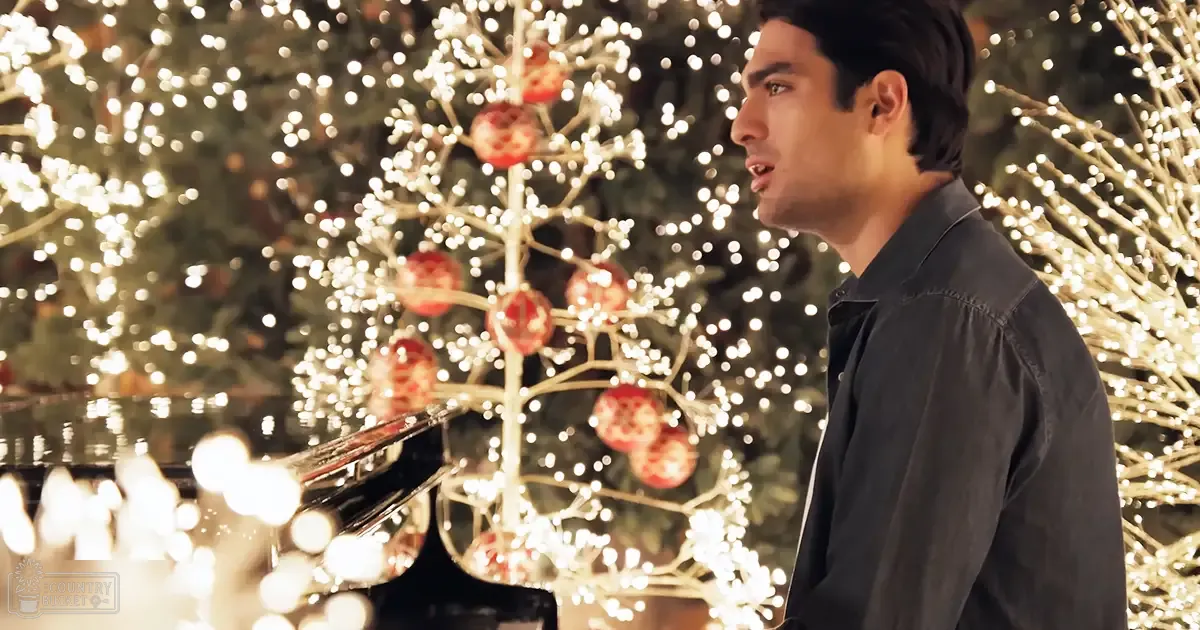 A young adult male in a relaxed fit, dark gray or black button-up shirt with festive Christmas decorations indoors.