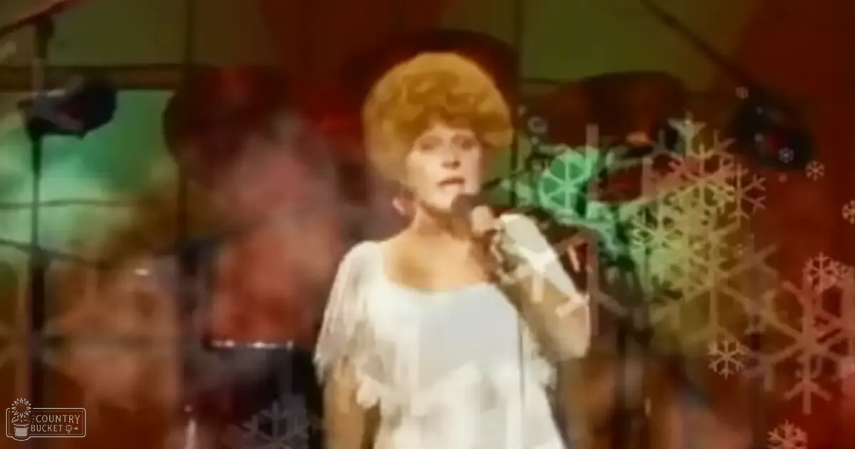 A female adult singer in a studio setting, wearing a white garment with fringe details and gloves, singing into a microphone.