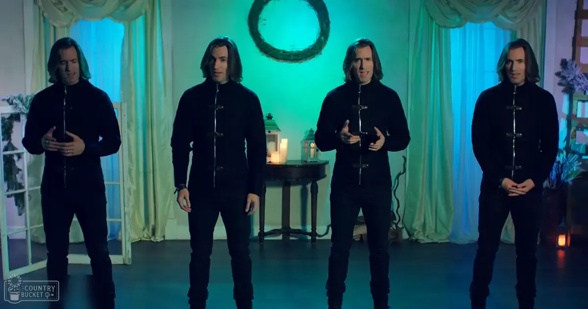 A group of adult males in black zip-up jackets performing on an indoor stage with decorative elements suggesting a festive theme.