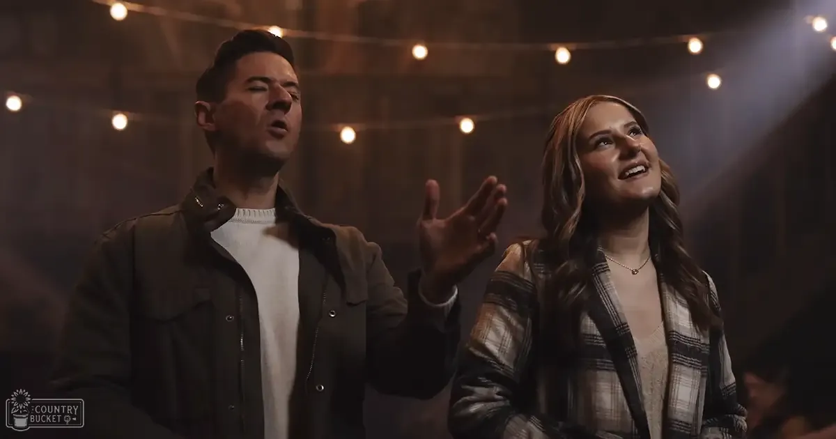 Young adult male and female in an indoor setting with wooden beams, string lights hanging from above.