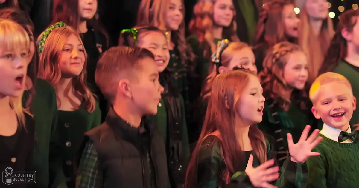 A group of children in performance attire on a stage with warm indoor lighting.
