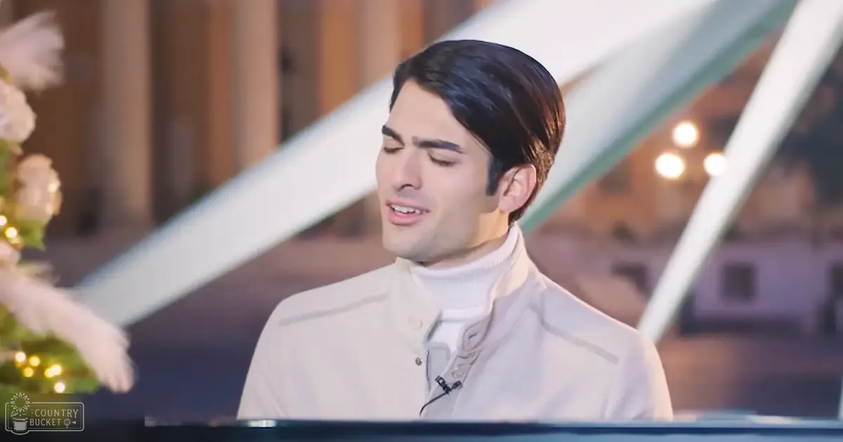 A young adult male wearing a fitted white turtleneck sweater in an indoor setting with modern architectural details.