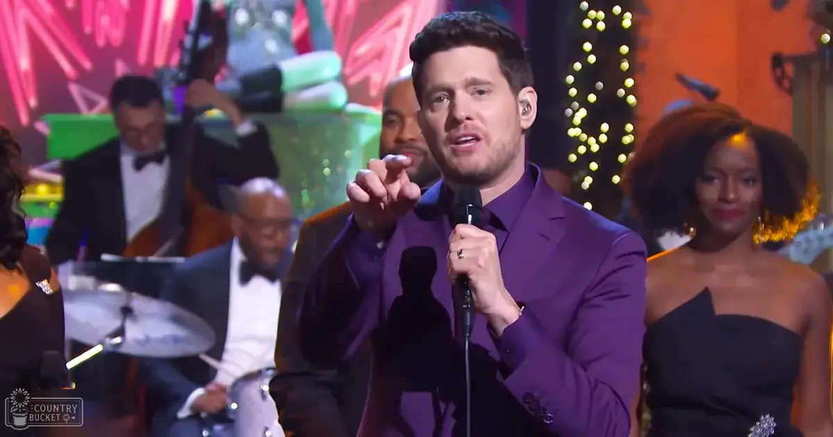 Adult male performer wearing a purple suit with bow tie at an indoor holiday-themed event.