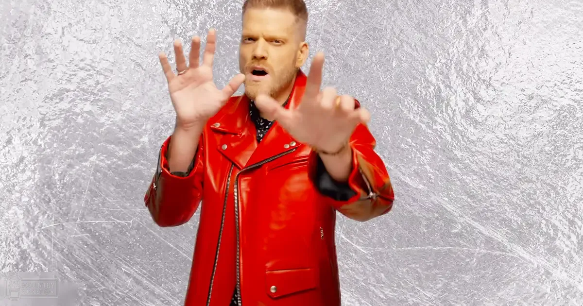 A young adult male model in a modern, glossy red leather jacket with rings on both ring fingers, set against an icy silver studio backdrop.