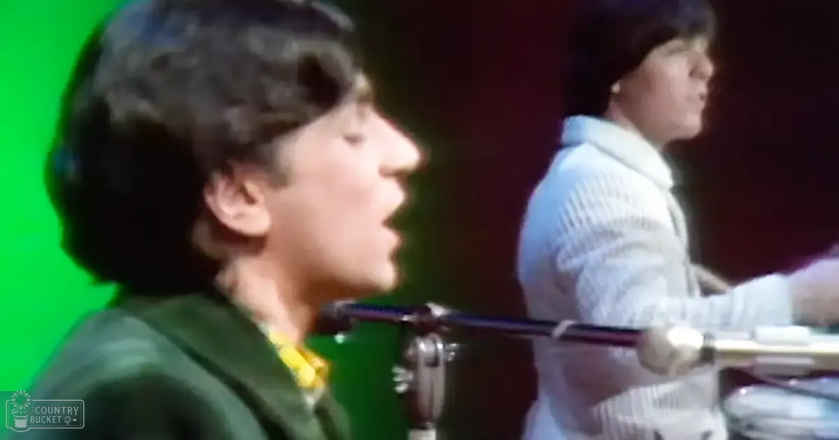 A young adult male singer wearing a dark green shirt with yellow collar, performing stage with another drummer in white striped shirt.