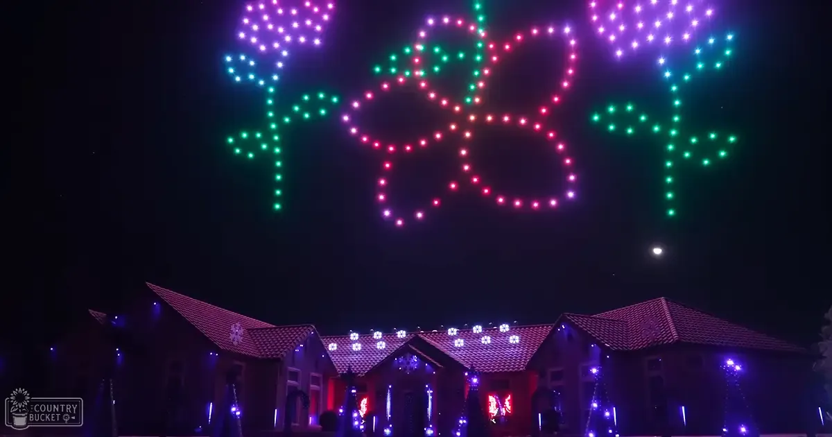A festive residential scene at night with a house adorned with Christmas decorations and drone lights spelling 'Merry' in the sky.