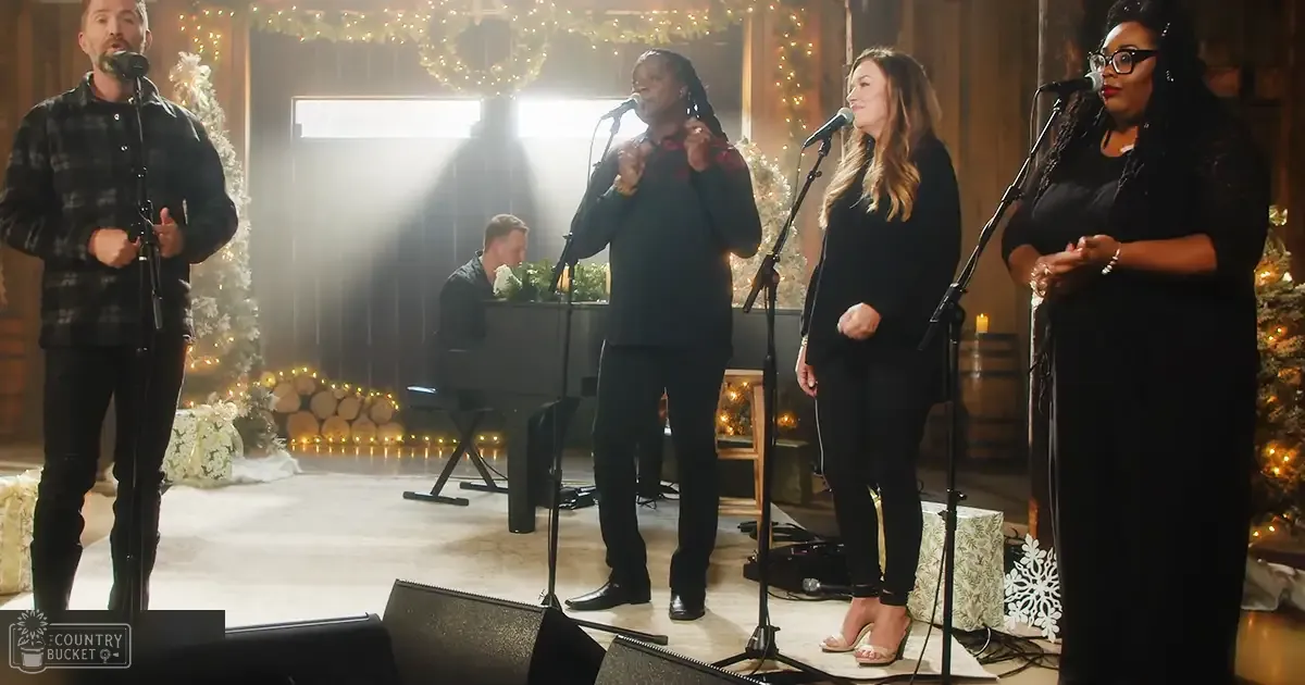 A small group of adults dressed in dark, relaxed-fit clothing performing indoors with holiday decorations around.