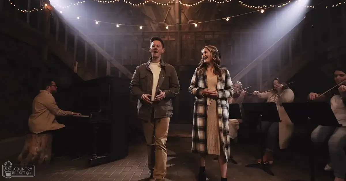 A musical performance in a rustic barn or theater-like setting with string lights and wooden beams during the evening.