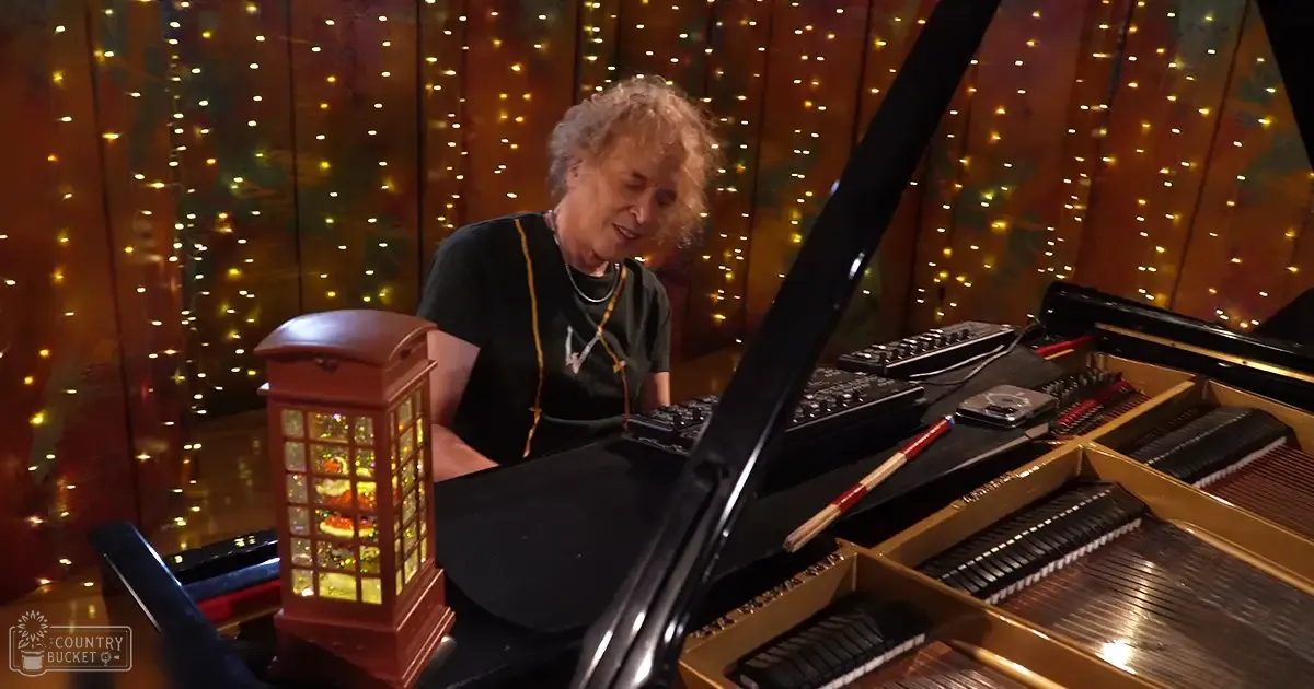 An older adult male playing a grand piano in a festive indoor setting with warm lighting.