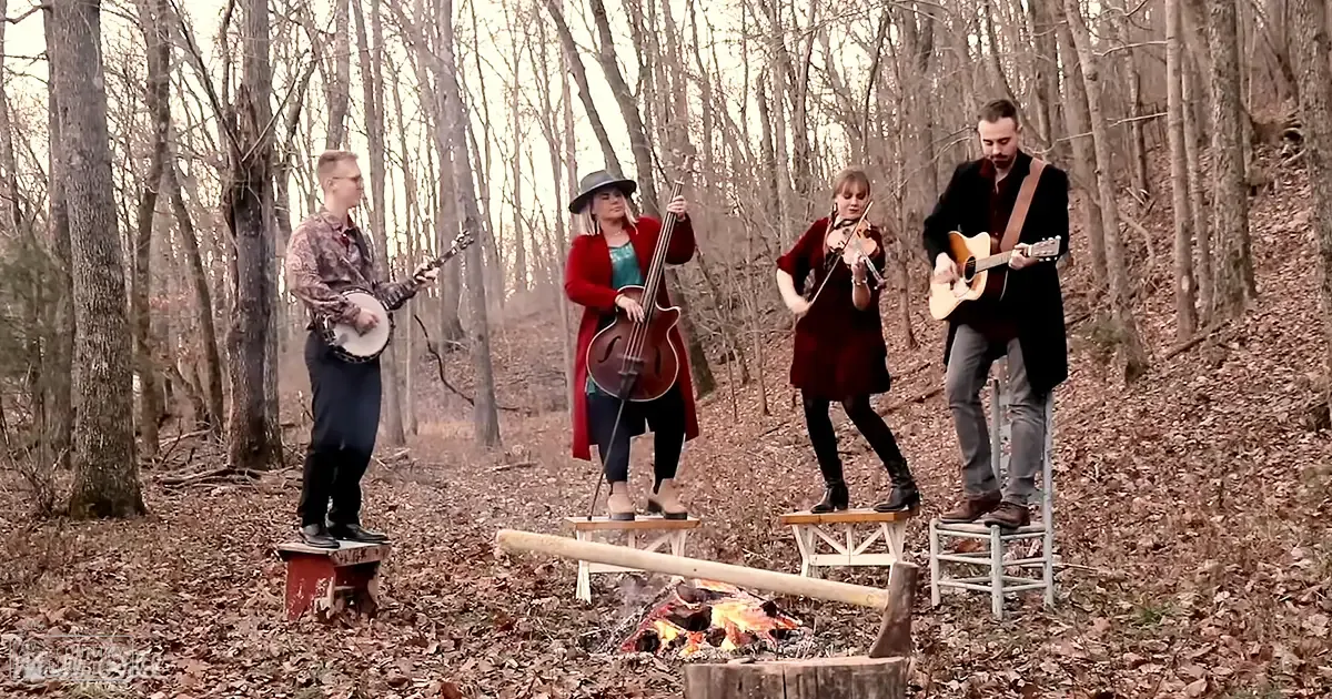 A small group of musicians performing outdoors in a wooded area with bare trees, late autumn or early winter setting, soft light.