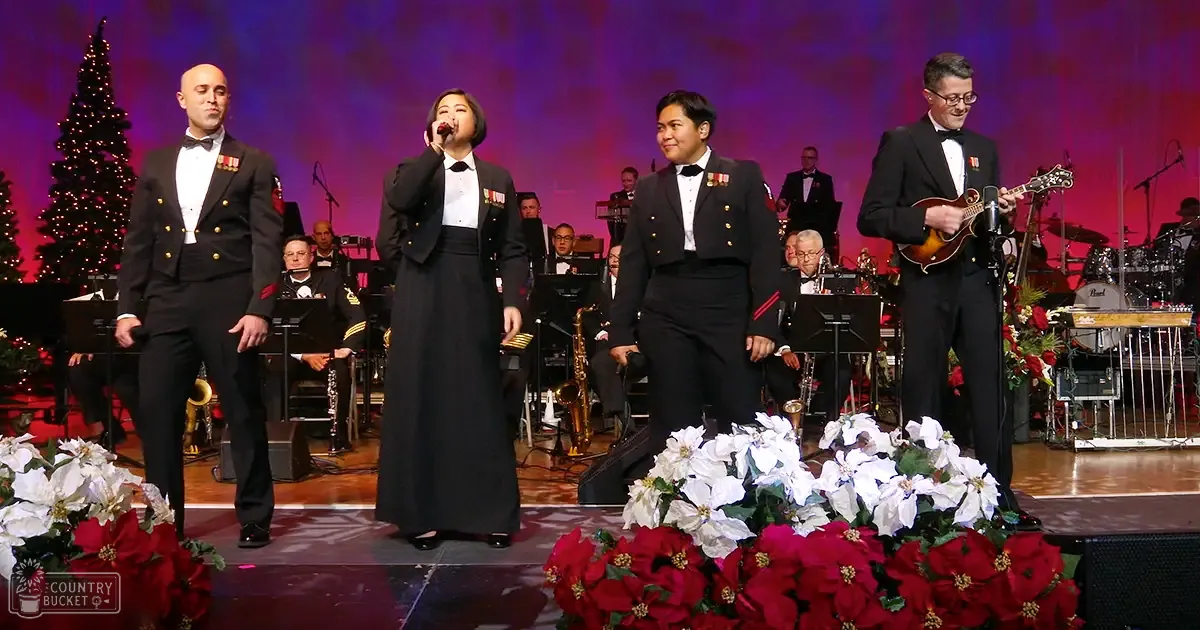 A Christmas concert scene with performers dressed in military-style tuxedos, set against a stage decorated with poinsettias and purple lighting.
