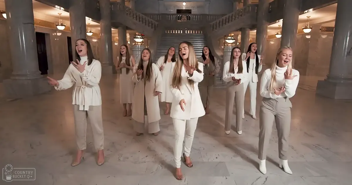 Young adult females performing in a grand indoor hall with large columns, marble floors, ornate lighting fixtures, and white clothing.