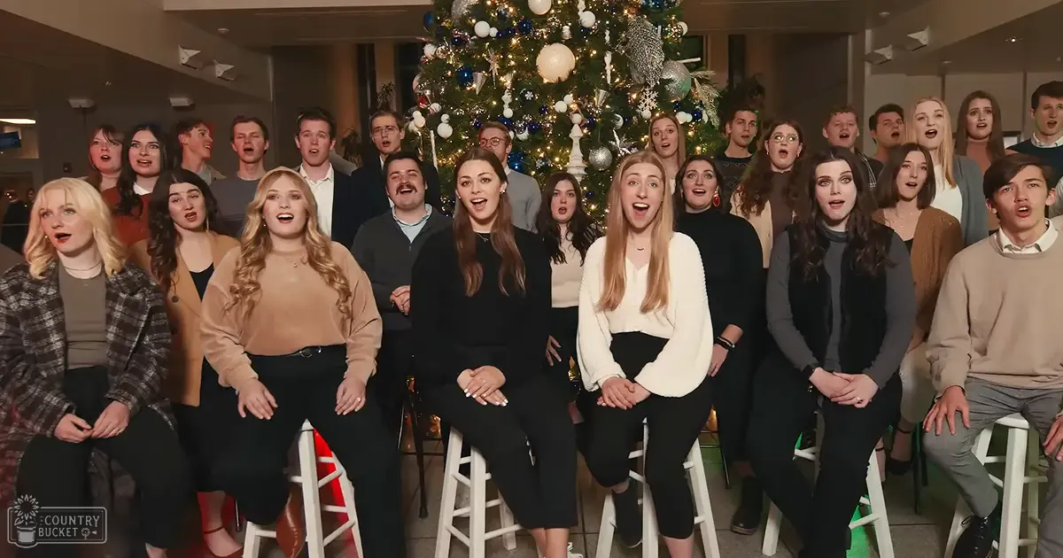 Group of young adults singing in front of a Christmas tree during an indoor event or gathering.