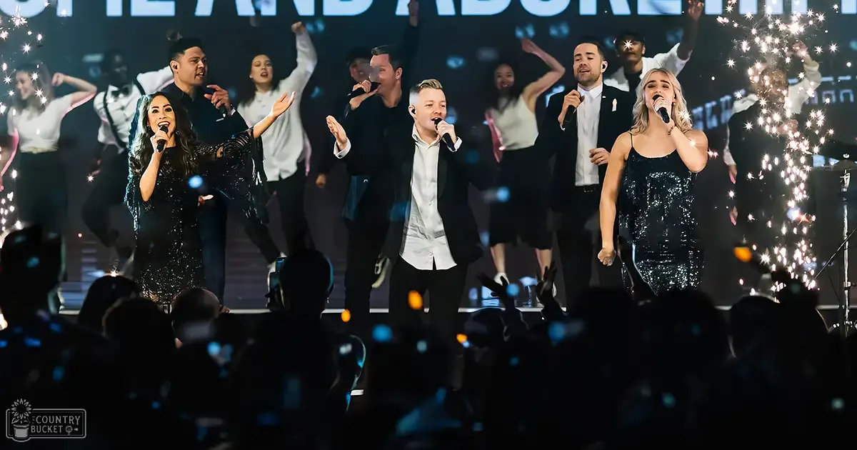 A performance group at a concert or event in an indoor venue with stage lighting and sparklers adding to the festive atmosphere.