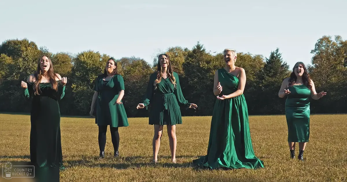 Five adult female singers in an open field with trees in the background during late afternoon light.