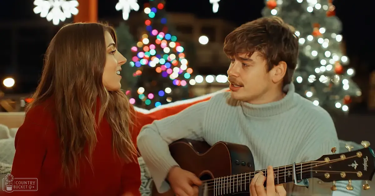 A couple singing in front of decorated Christmas trees at night, with a festive outdoor setting and artificial lighting creating a cozy holiday atmosphere.
