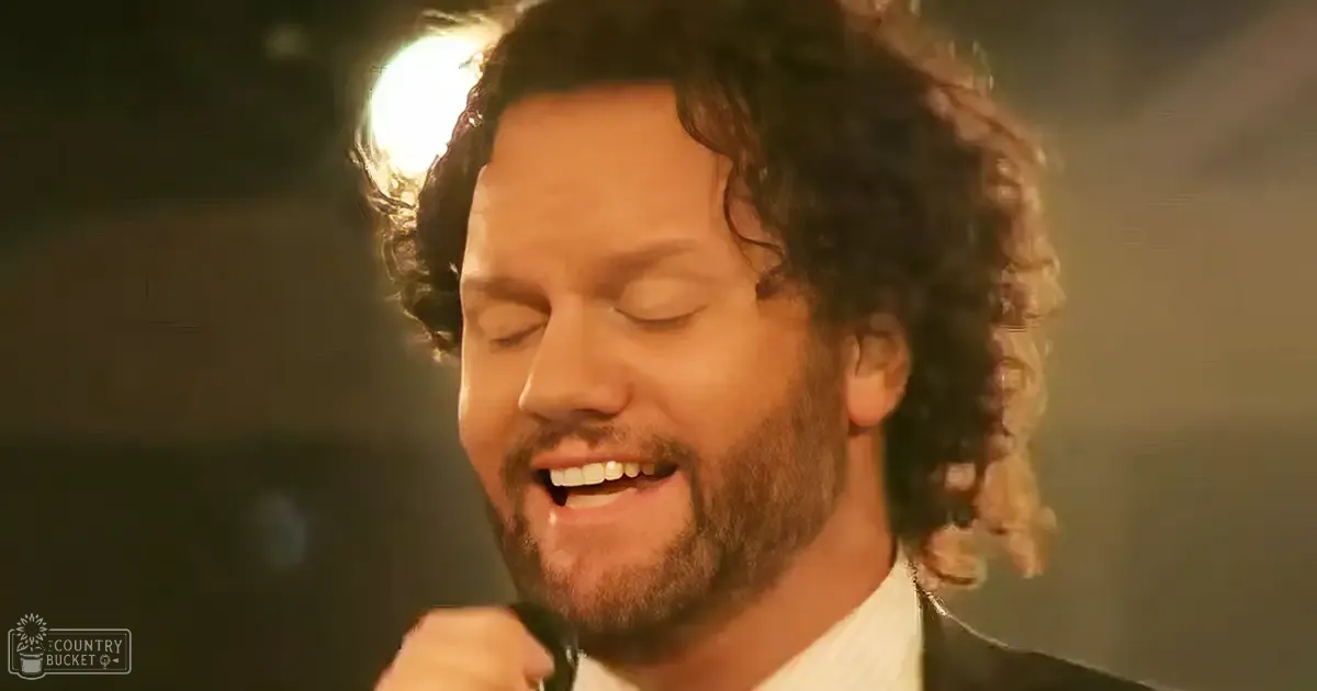 A male adult wearing a white collared shirt performs indoors under bright stage lighting.