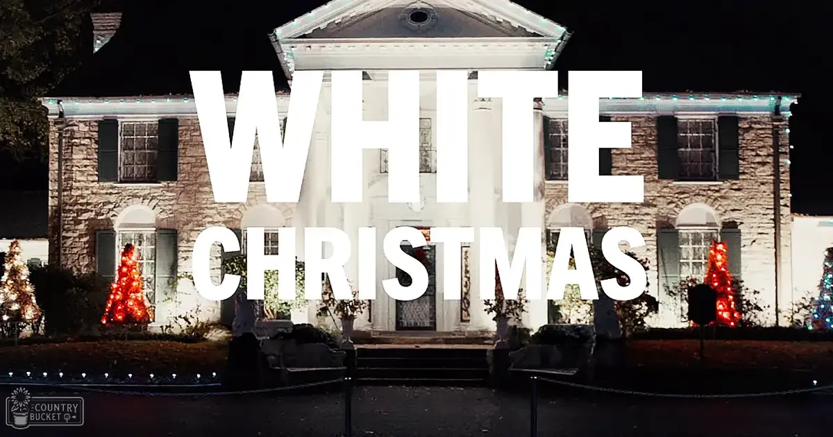 A large stone house with white columns, adorned with red Christmas lights, stands outdoors at dusk; 'WHITE CHRISTMAS' is written across its facade.