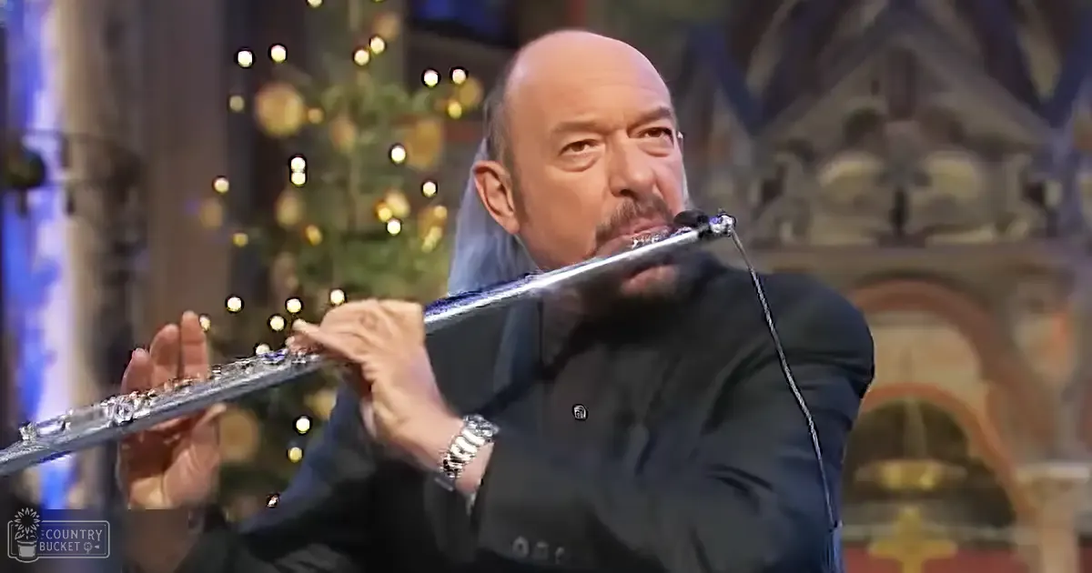 A middle-aged to older adult male plays a flute in an ornate church setting with festive lights, likely during Christmas season.