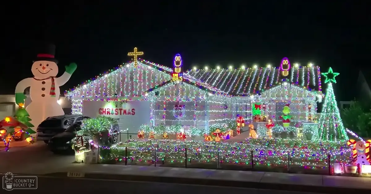 Festively decorated urban house with inflatable snowman, Grinch figure, and Christmas trees at night.