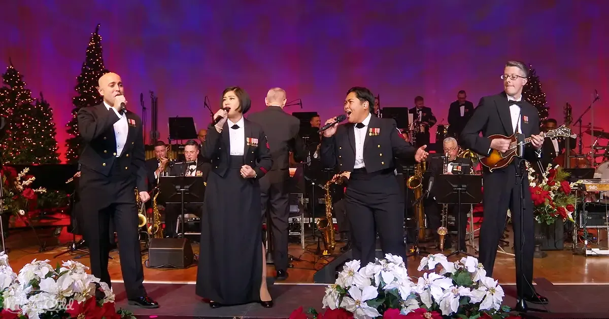 A holiday performance with a group singing and playing instruments indoors, decorated for Christmas.