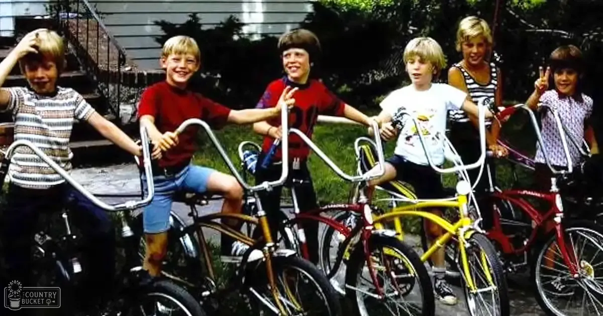 A group of children posing with bicycles in an outdoor residential setting, wearing casual summer clothing and enjoying a sunny day.