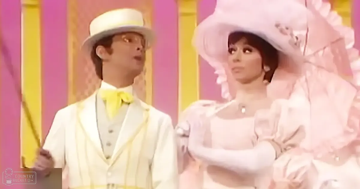 Two performers in mid-20th-century style attire on a brightly lit stage with a colorful backdrop, indicative of a theatrical or musical production.