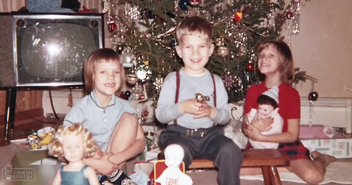 Children gather in front of a decorated Christmas tree, with a vintage television set to the side and wrapped presents beneath it. The scene is set indoors during daytime, likely in a living room.
