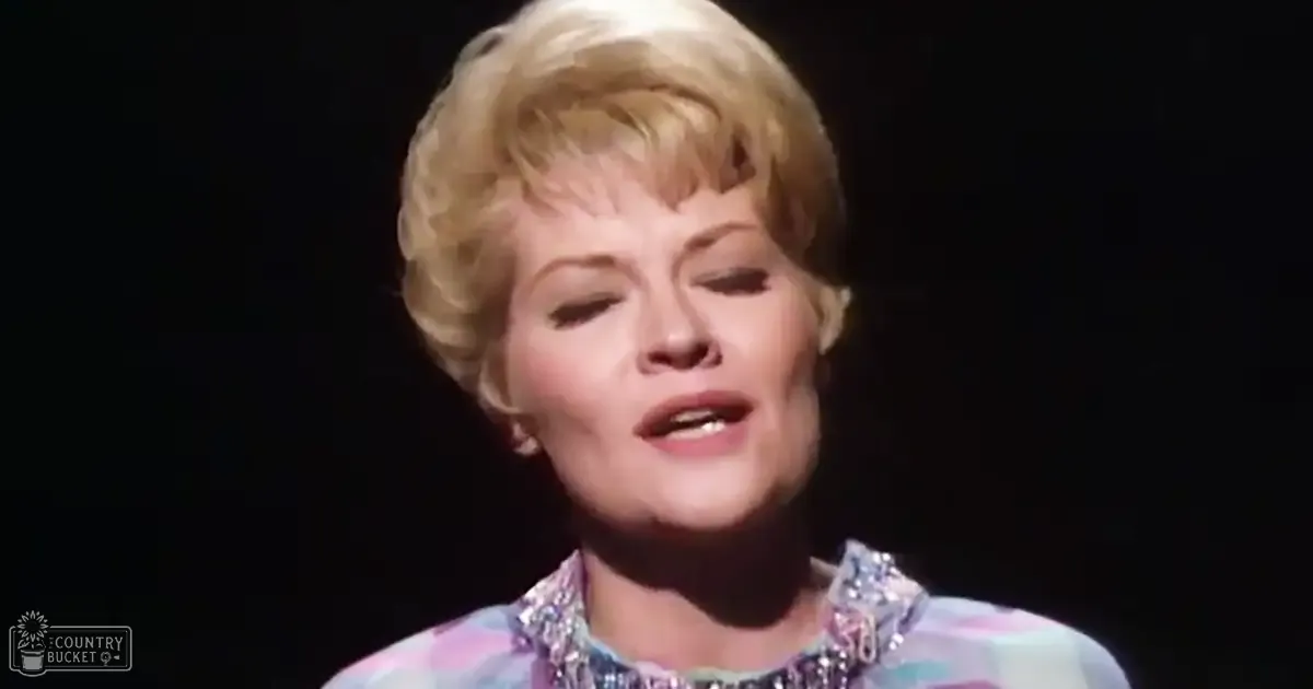 A middle-aged adult female wearing a detailed, patterned blouse or dress with intricate detailing on stage under dramatic lighting.