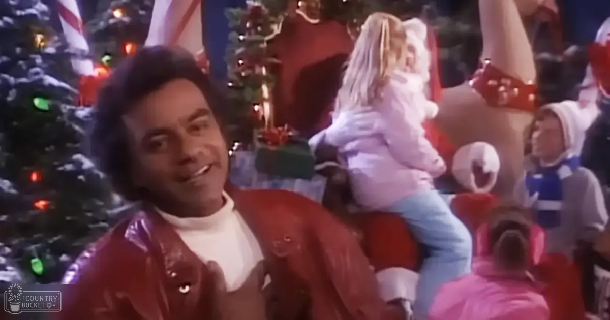 A festive Christmas indoor scene with an adult male in a red shiny jacket and white turtleneck sweater smiling, surrounded by children dressed in holiday attire on Santa's lap, and decorated trees with lights and ornaments, suggesting a warm winter day.