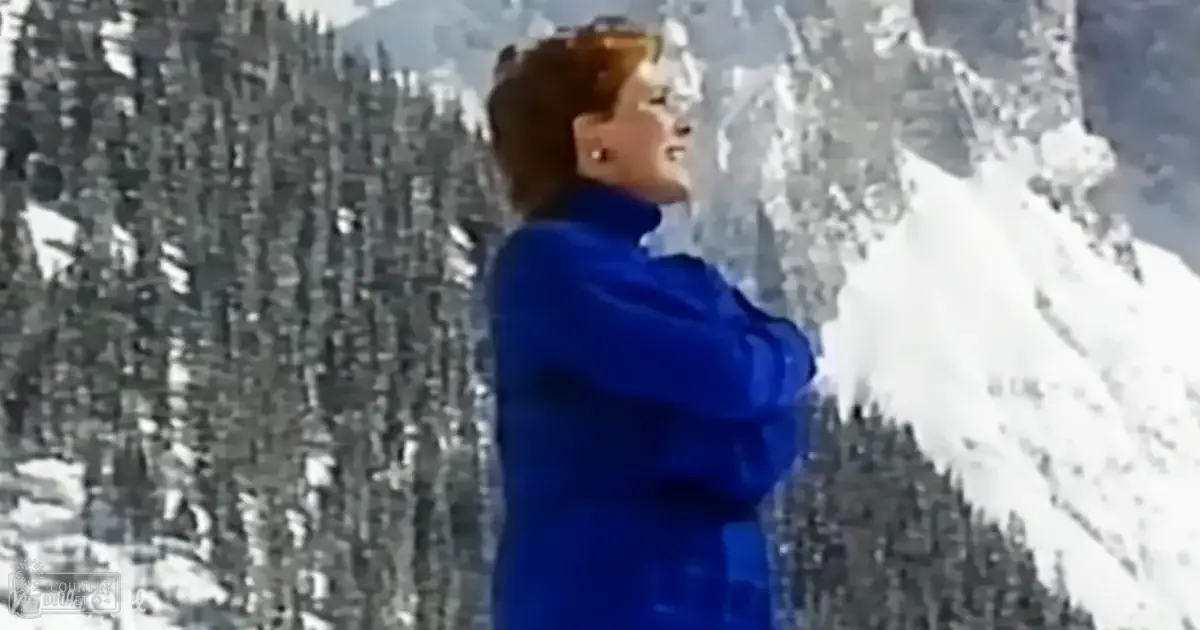 A young adult female stands on a snowy mountain landscape, wearing a bright blue jacket suitable for cold weather.