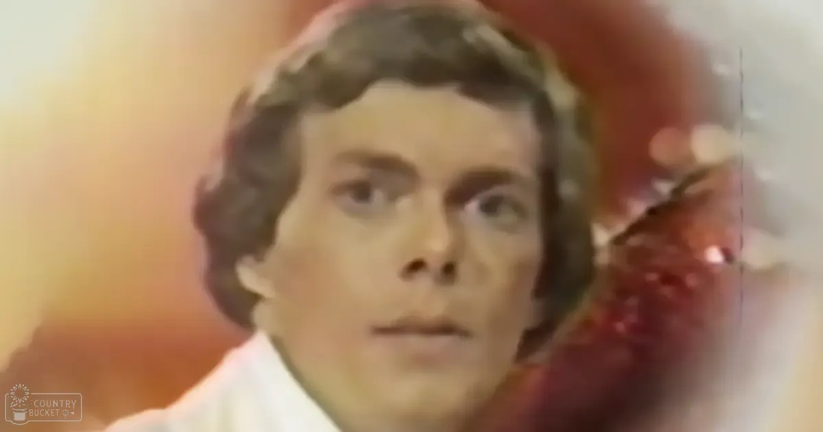 A young adult male wearing a white, high-collared garment indoors with warm tones and artificial lighting.
