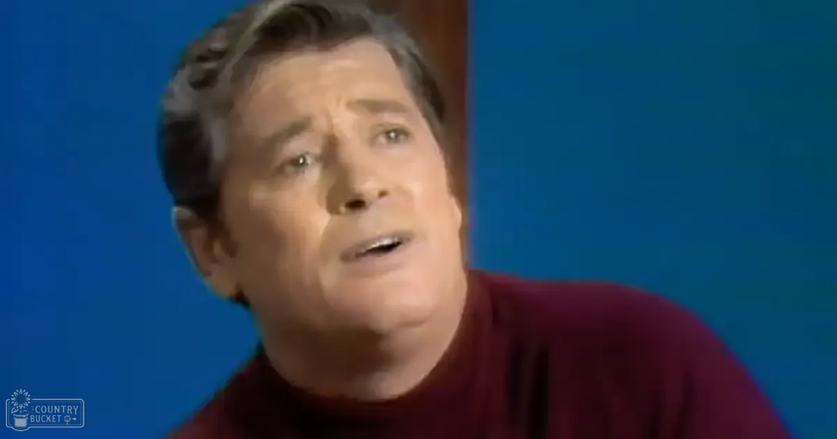 Middle-aged to older adult male in a studio setting, wearing a snug-fitting maroon turtleneck sweater with blue background.