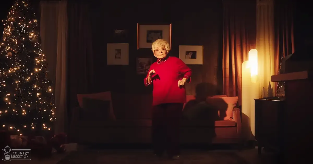 An older adult female in a cozy living room decorated for Christmas, wearing a red top with dark pants.