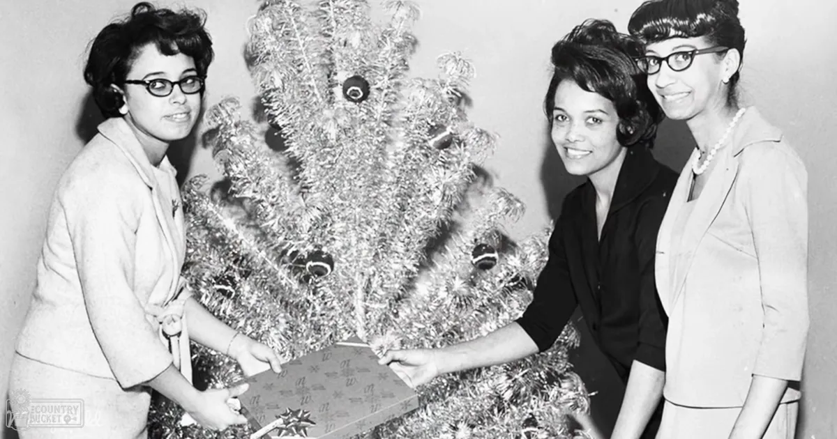 Young adult females dressed formally gather around a decorated Christmas tree indoors with wrapped gifts and jewelry.