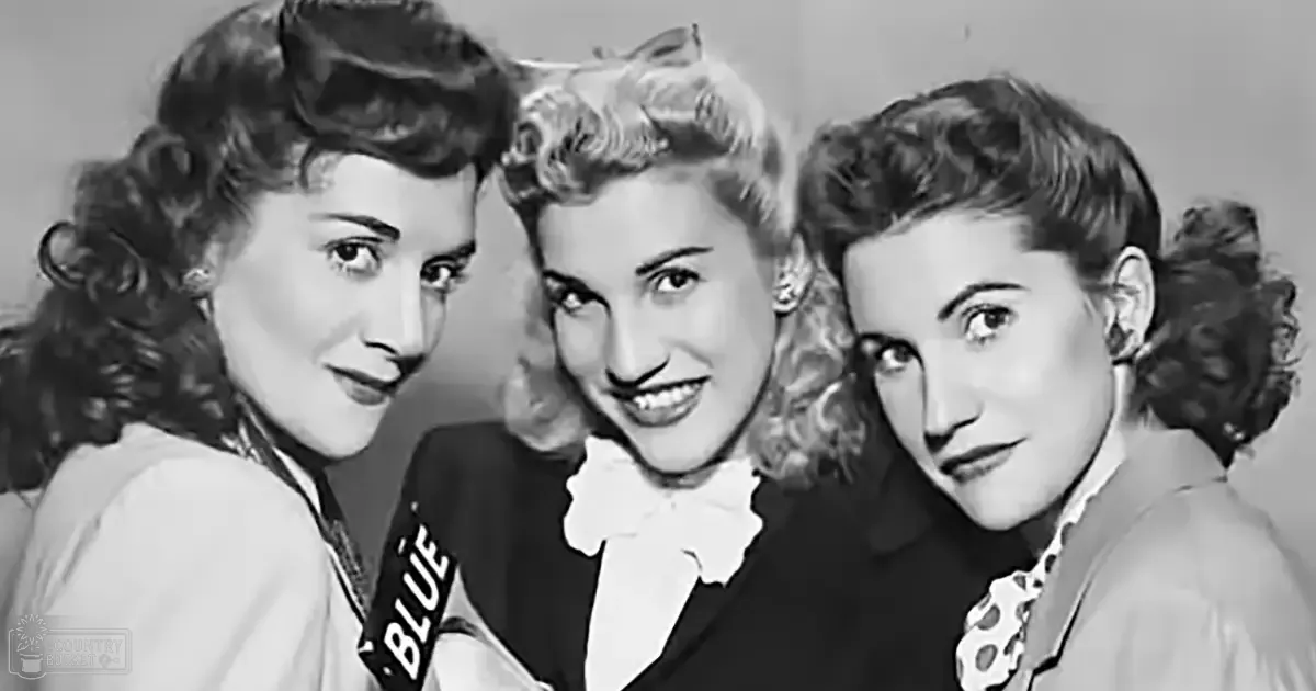 A group photo from the mid-20th century with three young adult women wearing light-colored tops in a studio setting, with even and bright lighting.