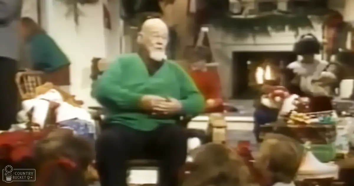 An older adult male wearing a green sweater, seated indoors in what appears to be a living room setting.