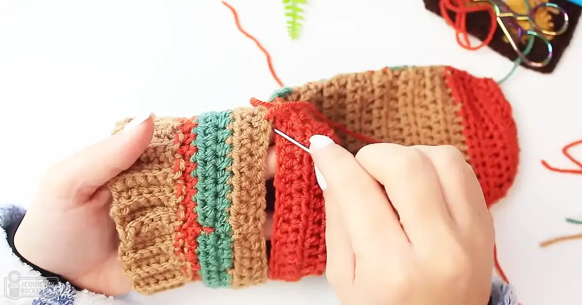 Adult female crocheting with brown and red yarn in an indoor crafting environment, focusing on the crochet project.