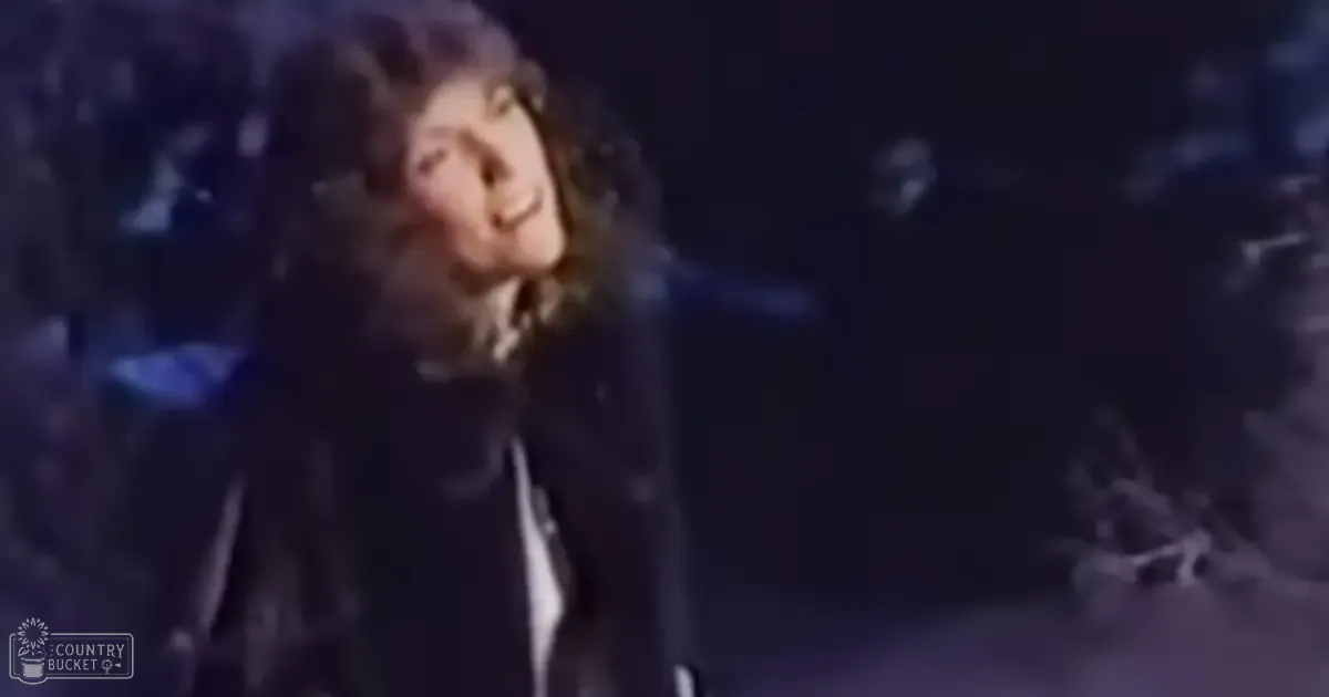 A young adult male singer performing in a dimly lit indoor venue, wearing a dark jacket and white shirt.