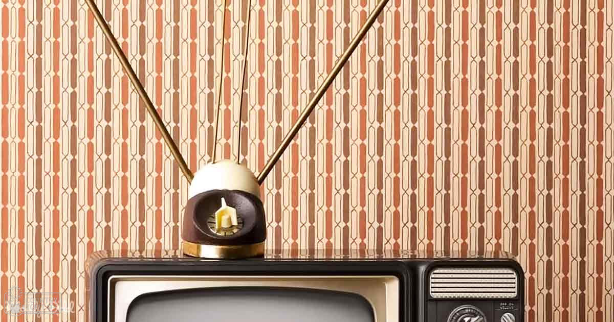 Vintage television set placed indoors against patterned wallpaper, even natural lighting suggests daytime