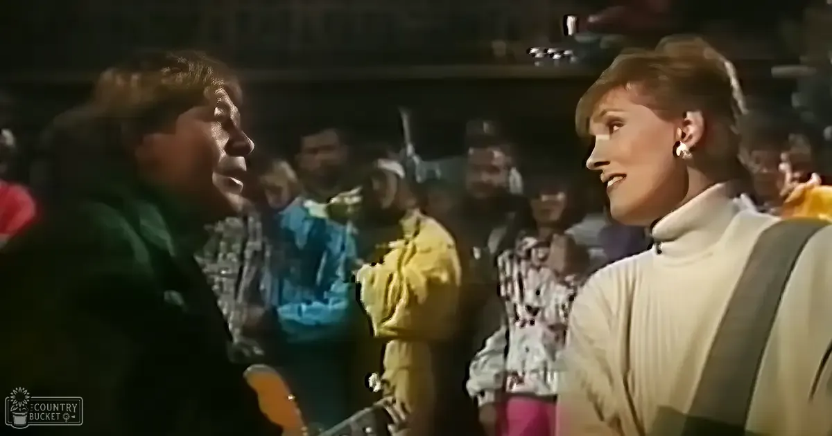 Adult male in dark jacket, female companion in white turtleneck sweater with large hoop earrings, setting appears to be a dimly lit bar or nightclub with jukebox and other patrons visible.