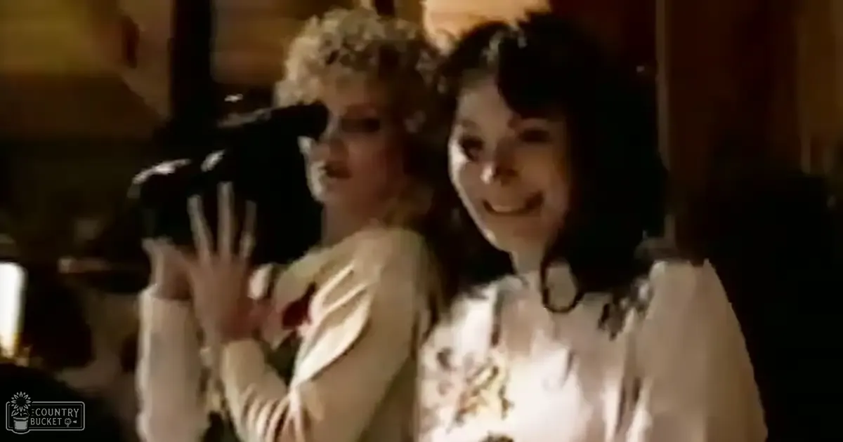 Two young adult females in an indoor setting wearing white blouses; one with lace details and cotton or linen blend fabric, the other with a floral pattern and light fabric such as cotton or silk.
