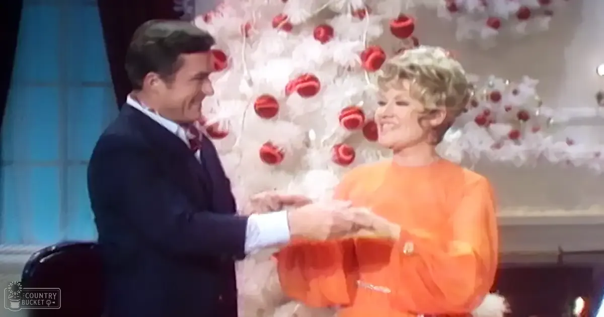A festive holiday scene with two adults in front of a decorated Christmas tree, wearing mid-20th century attire.