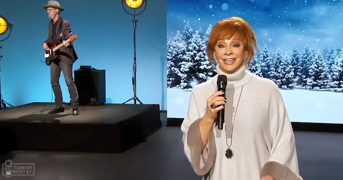 An adult male singer and an older female performer stand indoors with a snowy forest backdrop, suggesting a winter-themed performance setting.