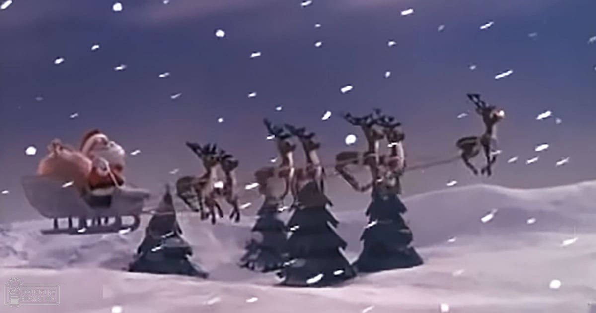 Several reindeer pulling a sleigh in a snowy landscape with evergreen trees and falling snowflakes, suggesting early morning or late evening light.