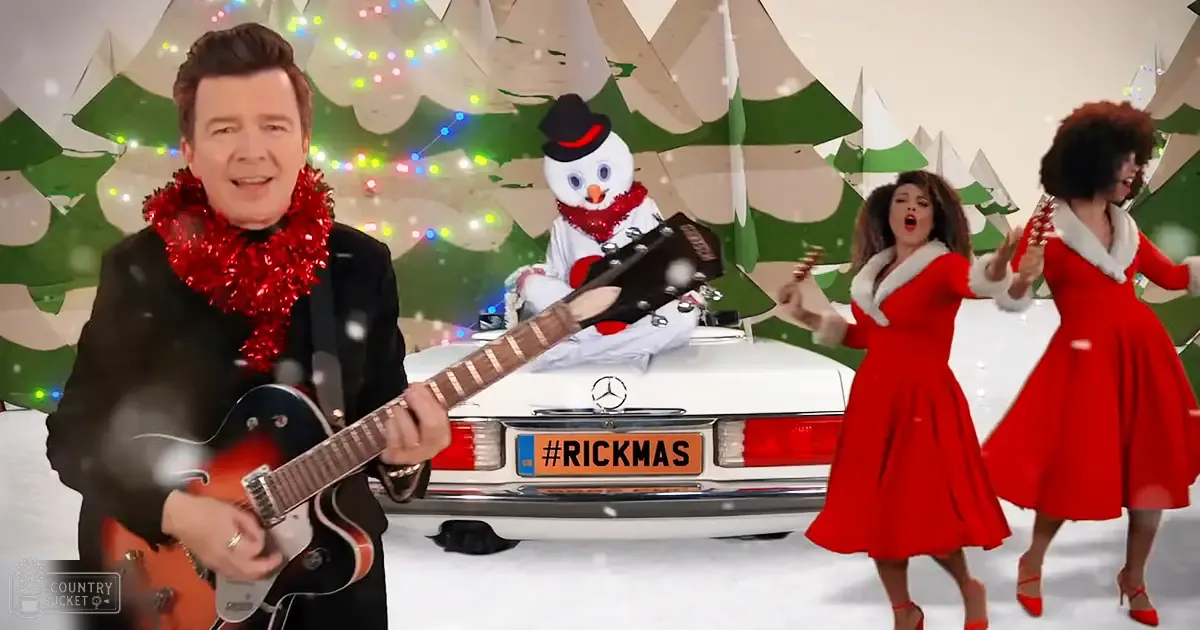 A middle-aged male performer wearing a black suit and red scarf, holding an electric guitar, stands with two female adults in festive red dresses. A white Mercedes-Benz car decorated for Christmas is parked nearby.