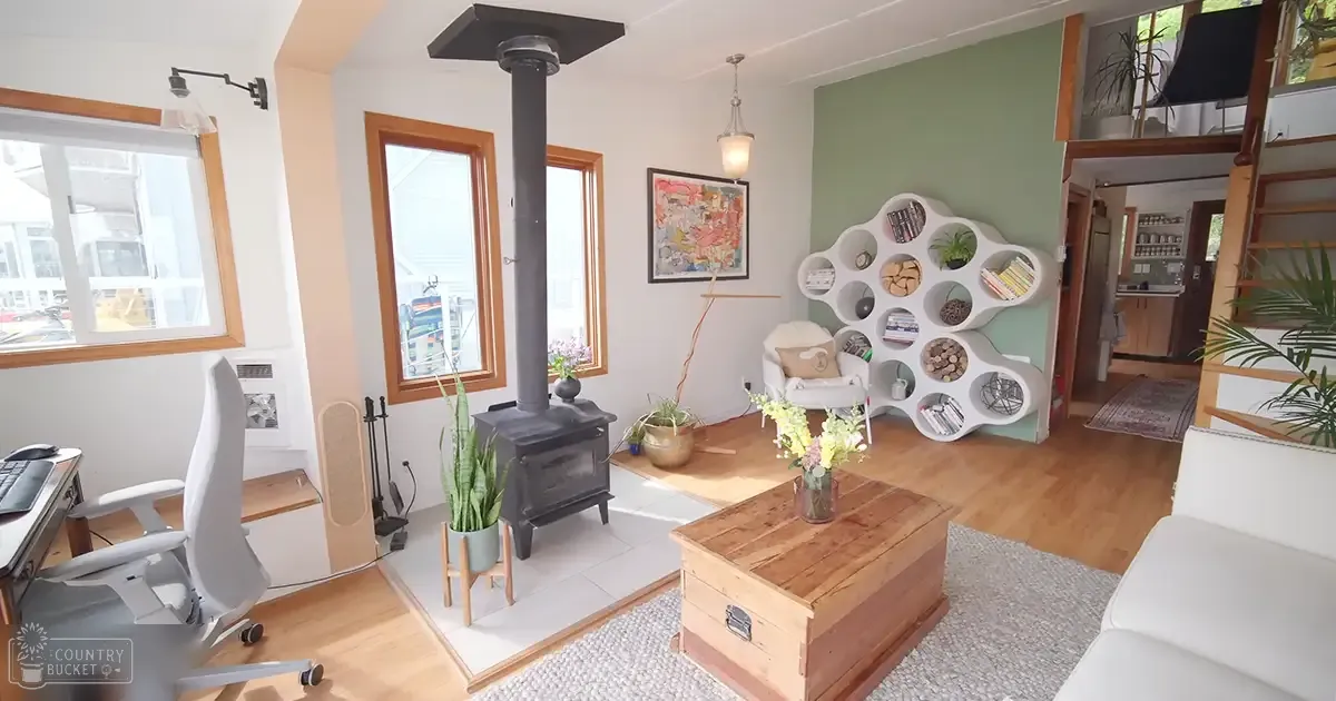 A cozy home interior with white office chair, wooden coffee table, black wood-burning stove, and bookshelf in a well-lit room.