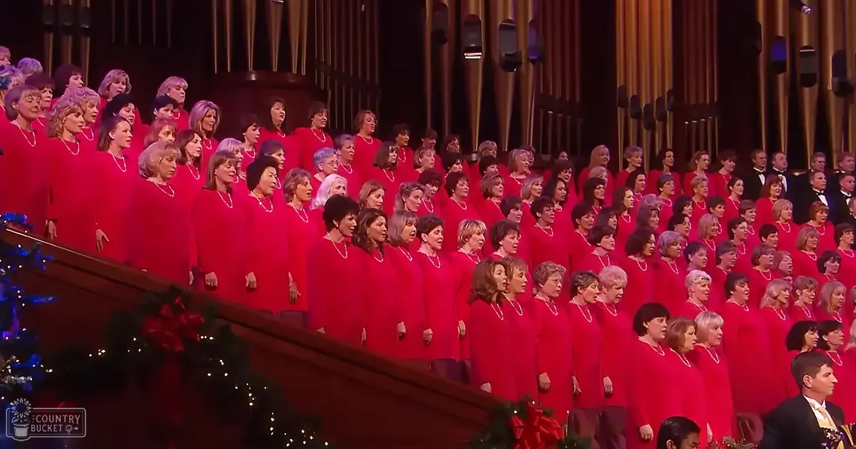 A choir in red robes performing at a performance hall with Christmas decorations and wooden pipes in the background.