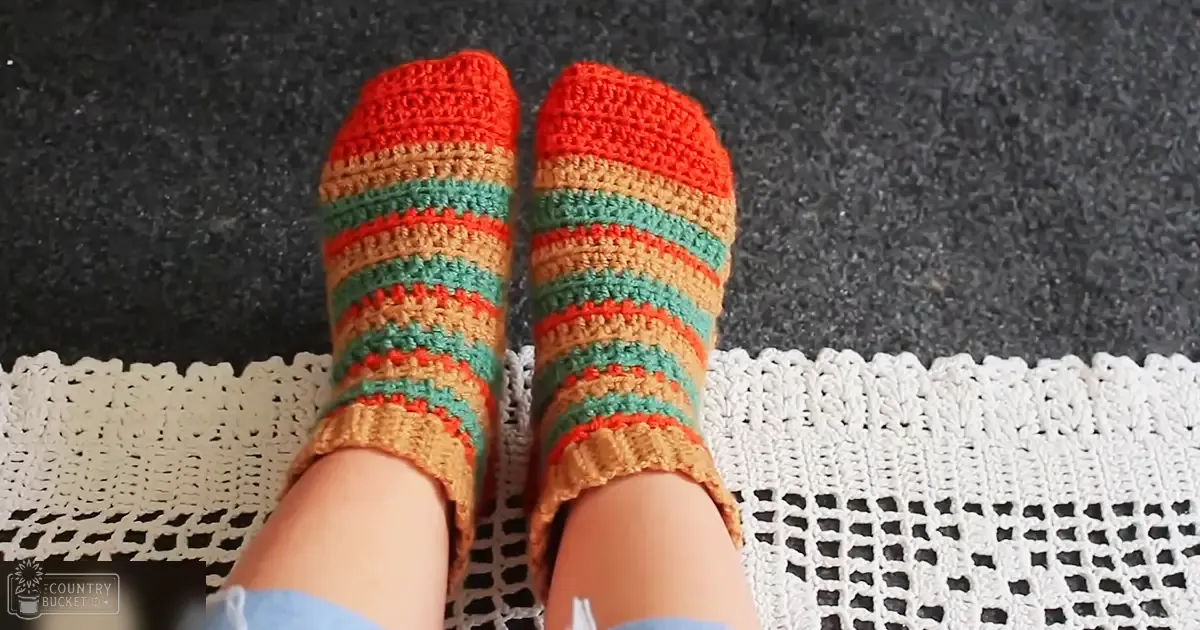 A cozy indoor scene with crocheted socks, light blue jeans, and a white doily on dark carpeted floor.
