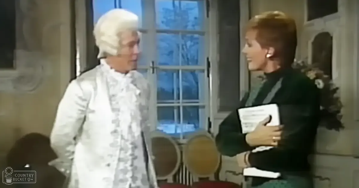 Historical reenactment scene with two individuals, one dressed in a white 18th-century costume and powdered wig, another wearing modern attire holding papers, set indoors with wooden barrels and a window.